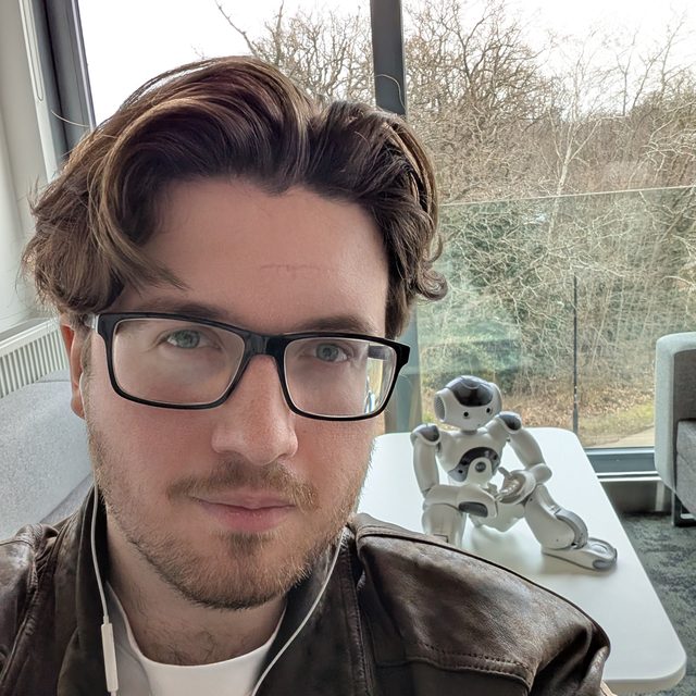 James Stedman, with a small humanoid robot on the table behind him